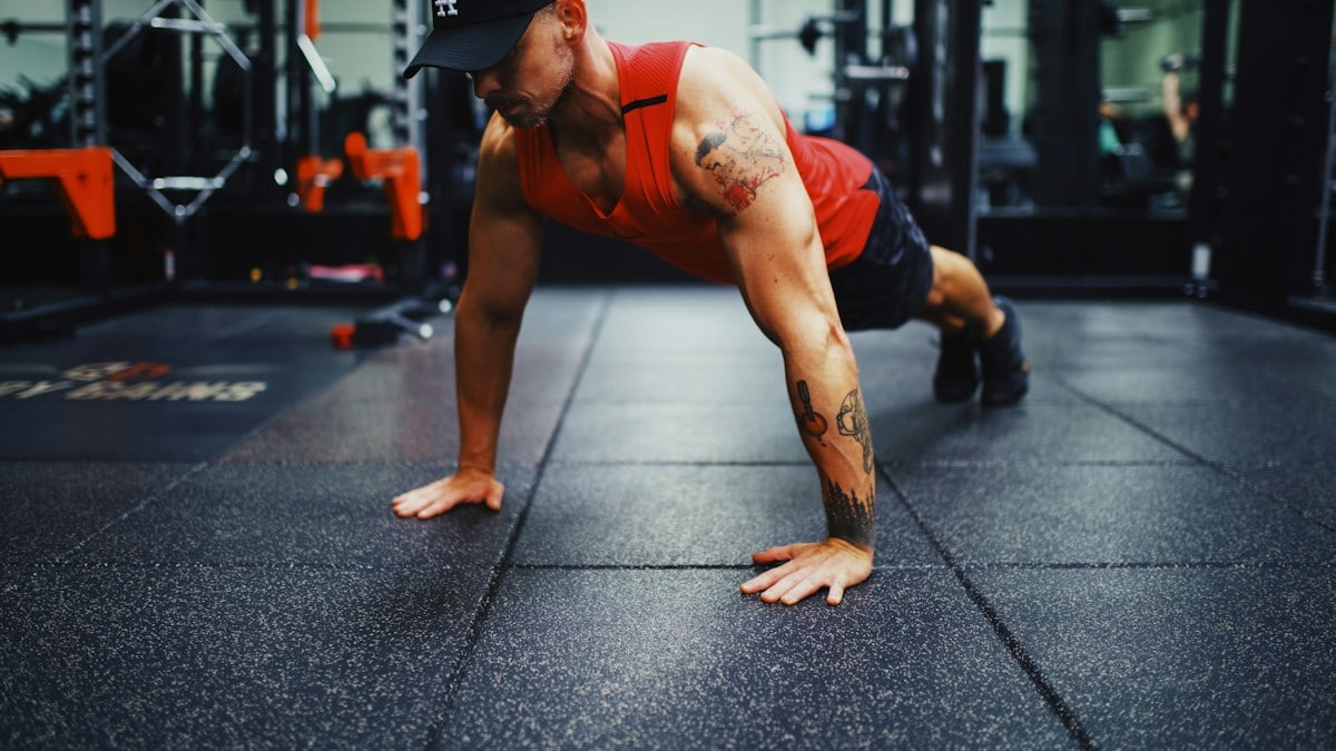 man in red tank top and black shorts doing push up on the street